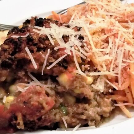 Serving of stuffed egg[lant alongside serving of spaghetti noodles with shredded parmesan cheese.