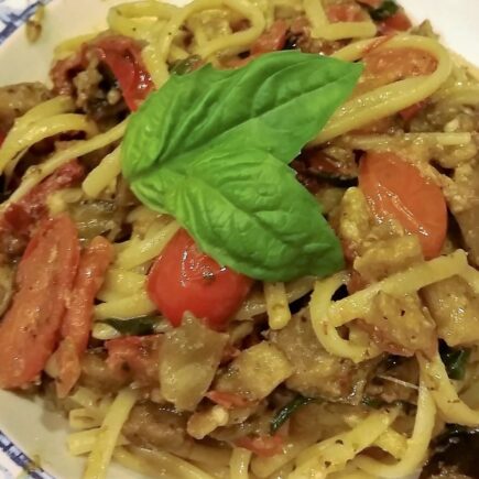 Extreme close-up of a single serving of spaghetti noodles and eggplant ragout in white bowls on wooden tabletop
