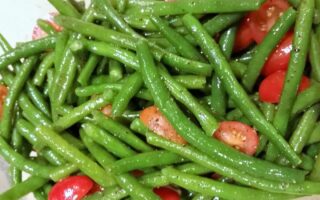 Close-up of blanched green beans and tomatoes dressed in oil and seasonings.