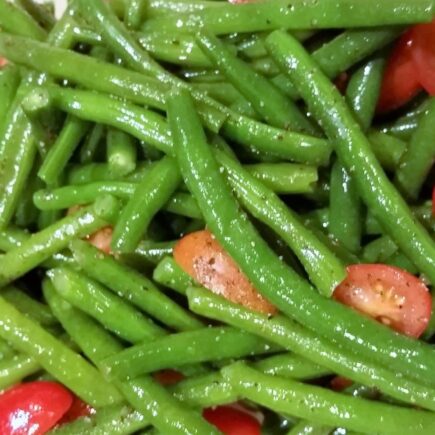 Close-up of blanched green beans and tomatoes dressed in oil and seasonings.