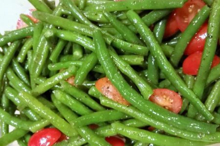 Close-up of blanched green beans and tomatoes dressed in oil and seasonings.
