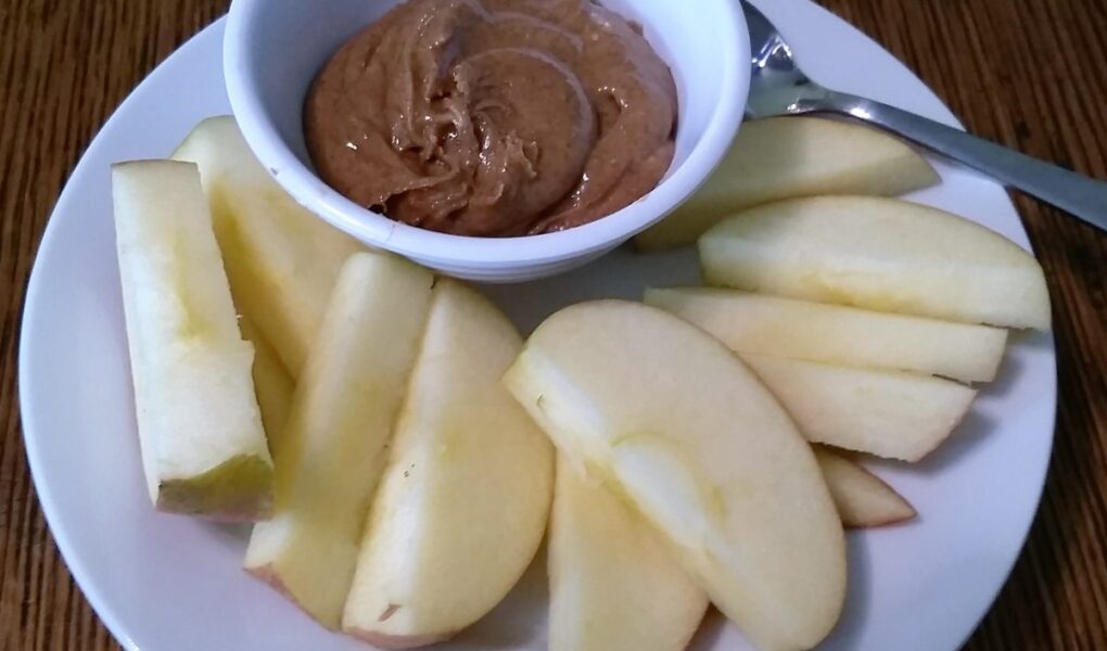Bowl of spiced almond butter served with apple slices on a dessert plate