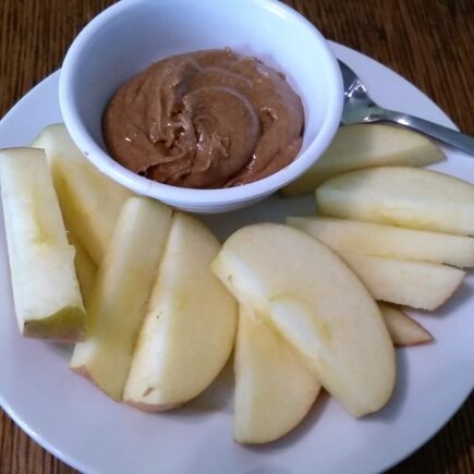 Bowl of spiced almond butter served with apple slices on a dessert plate