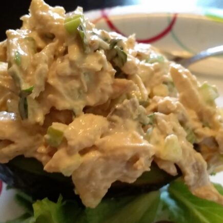 Finished chicken salad served on half an avocado on paper plate
