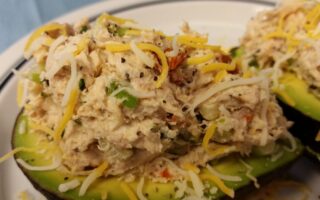 Close-up of finished cheicken salad served on two avocado halves and topped with additional shredded cheese served on a white plate