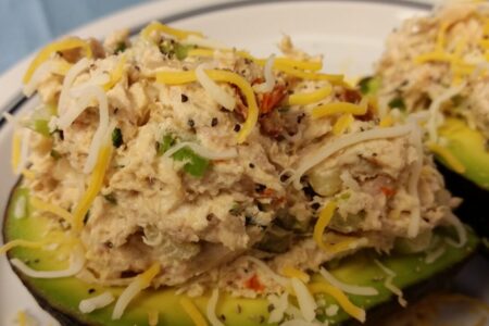 Close-up of finished cheicken salad served on two avocado halves and topped with additional shredded cheese served on a white plate