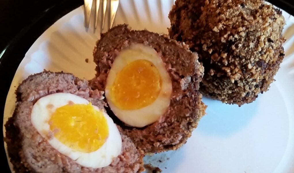 Two scotch eggs served on white paper plate, one cut in half