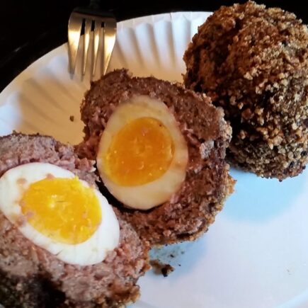 Two scotch eggs served on white paper plate, one cut in half