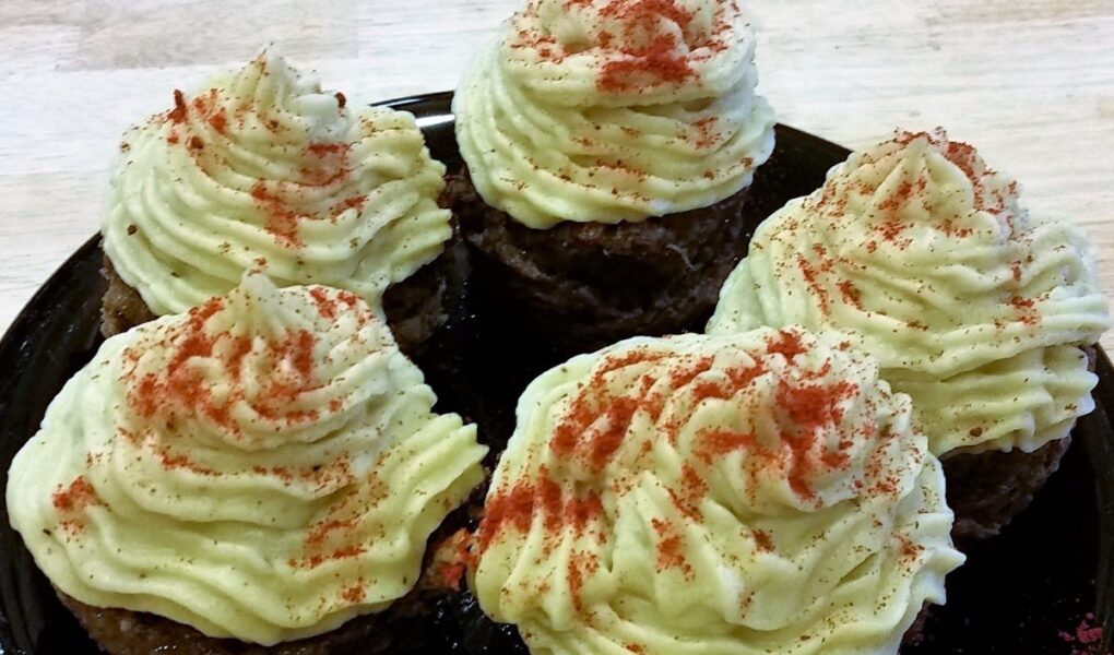 Close-up of black serving plate with five finished liver cupcakes topped with decorative mashed yams and sprinkled with paprika