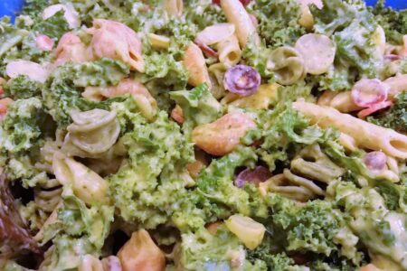 Close up of salad showing kale, dressing along with penne and spiral pasta and grapes